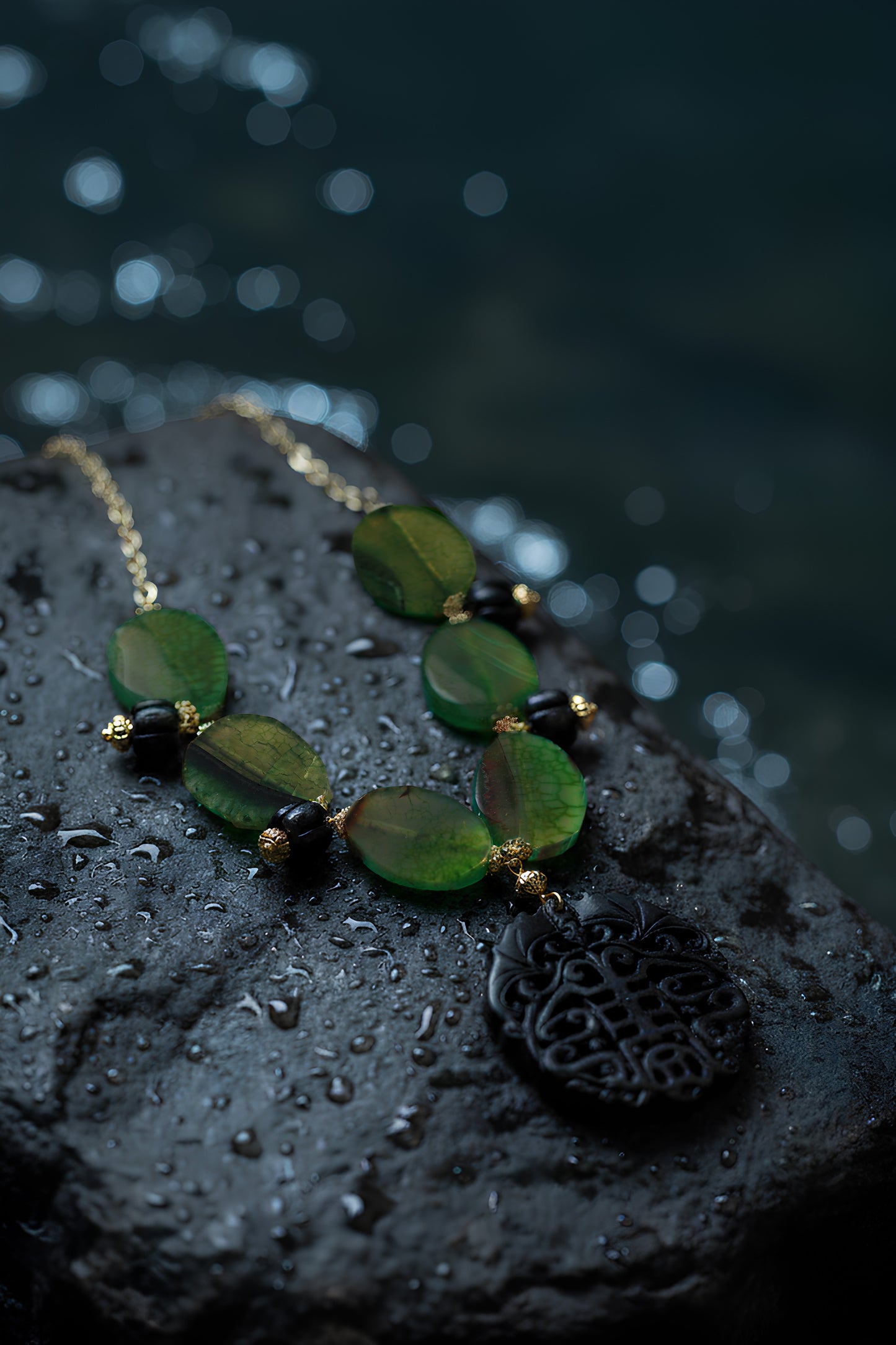 Handcrafted artisan green agate necklace with a carved black jade pendant on a dark surface with sea in the background