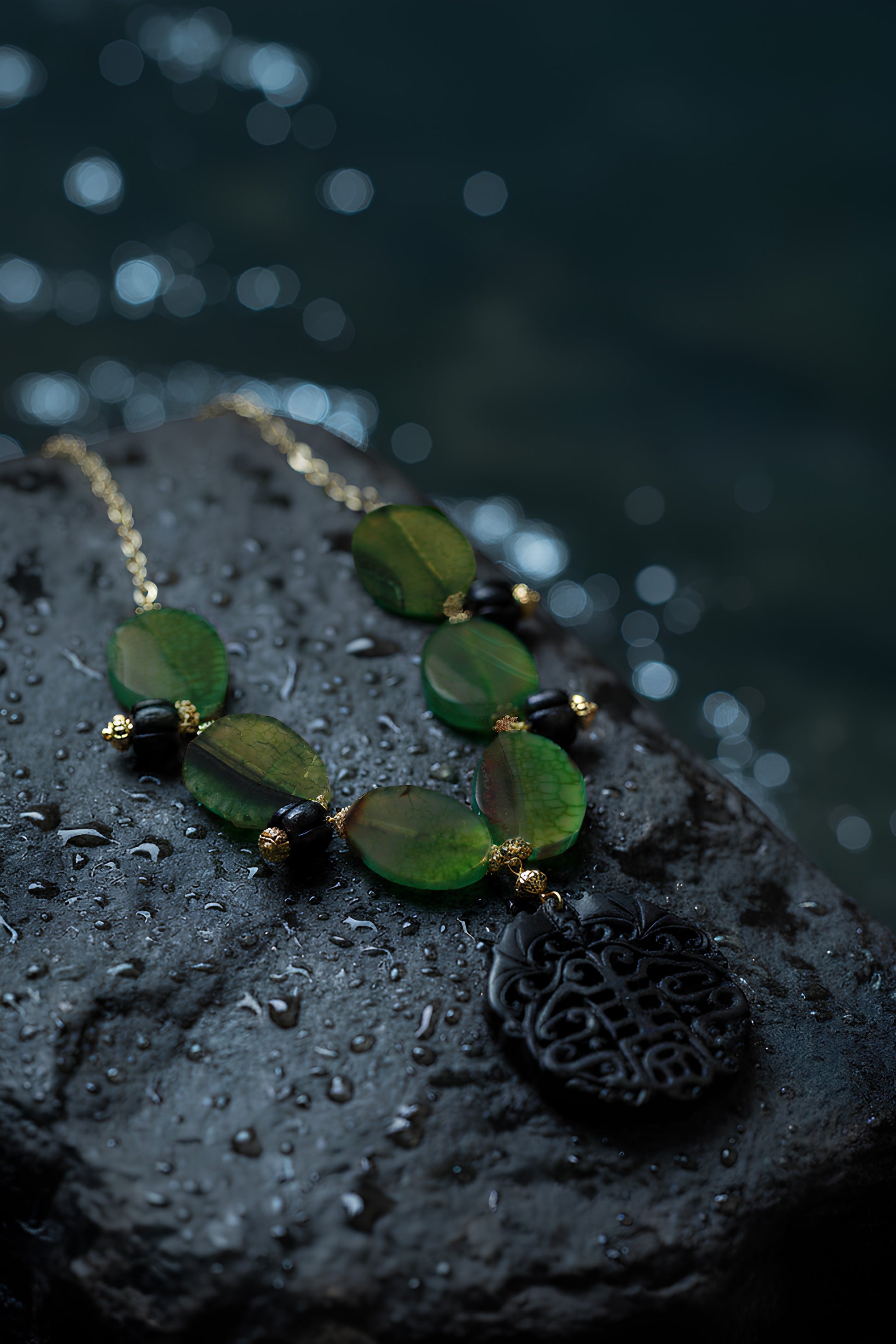 Handcrafted artisan green agate necklace with a carved black jade pendant on a dark surface with sea in the background